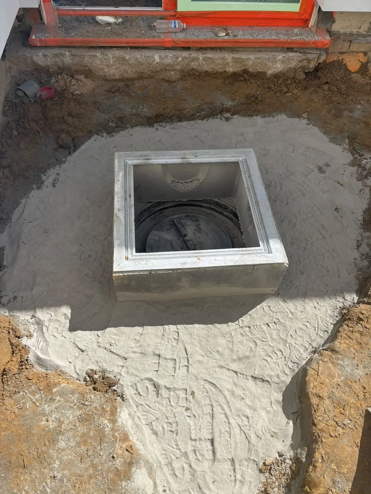 Betonnen toezichtsput ingegraven in zand voor de gevel in Oostakker